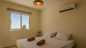 Ein Hotelzimmer mit Bett, zwei zusammengerollten Handtüchern, einem Fenster mit Aussicht, einer Klimaanlage und einer grünen Lampe auf einem Nachttisch.