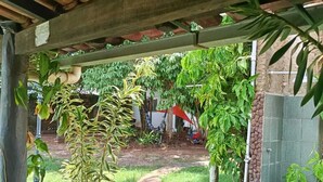 A covered garden area with a brick pathway, various plants, and a view of a residential area in the background. - Namaste Camping Suite (Aruanã)