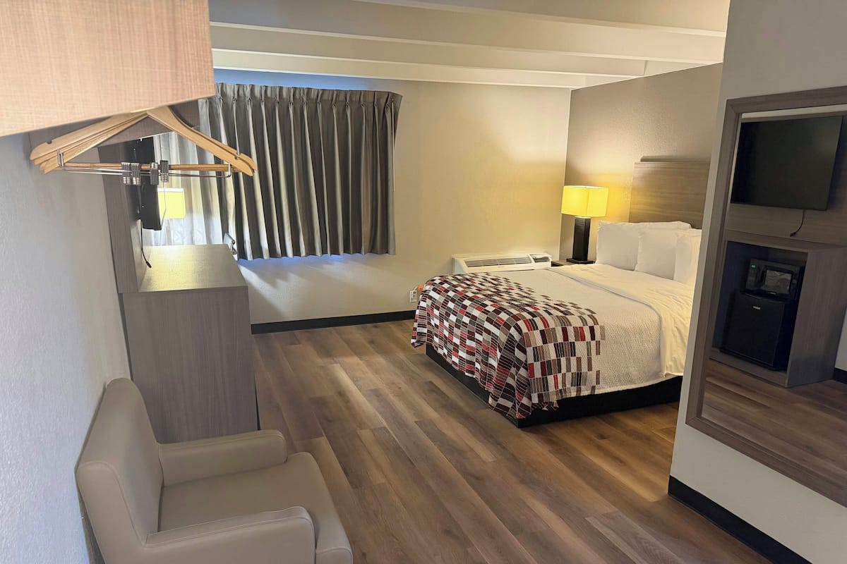 A hotel room with a bed, a desk, a chair, a TV, and a window with curtains.