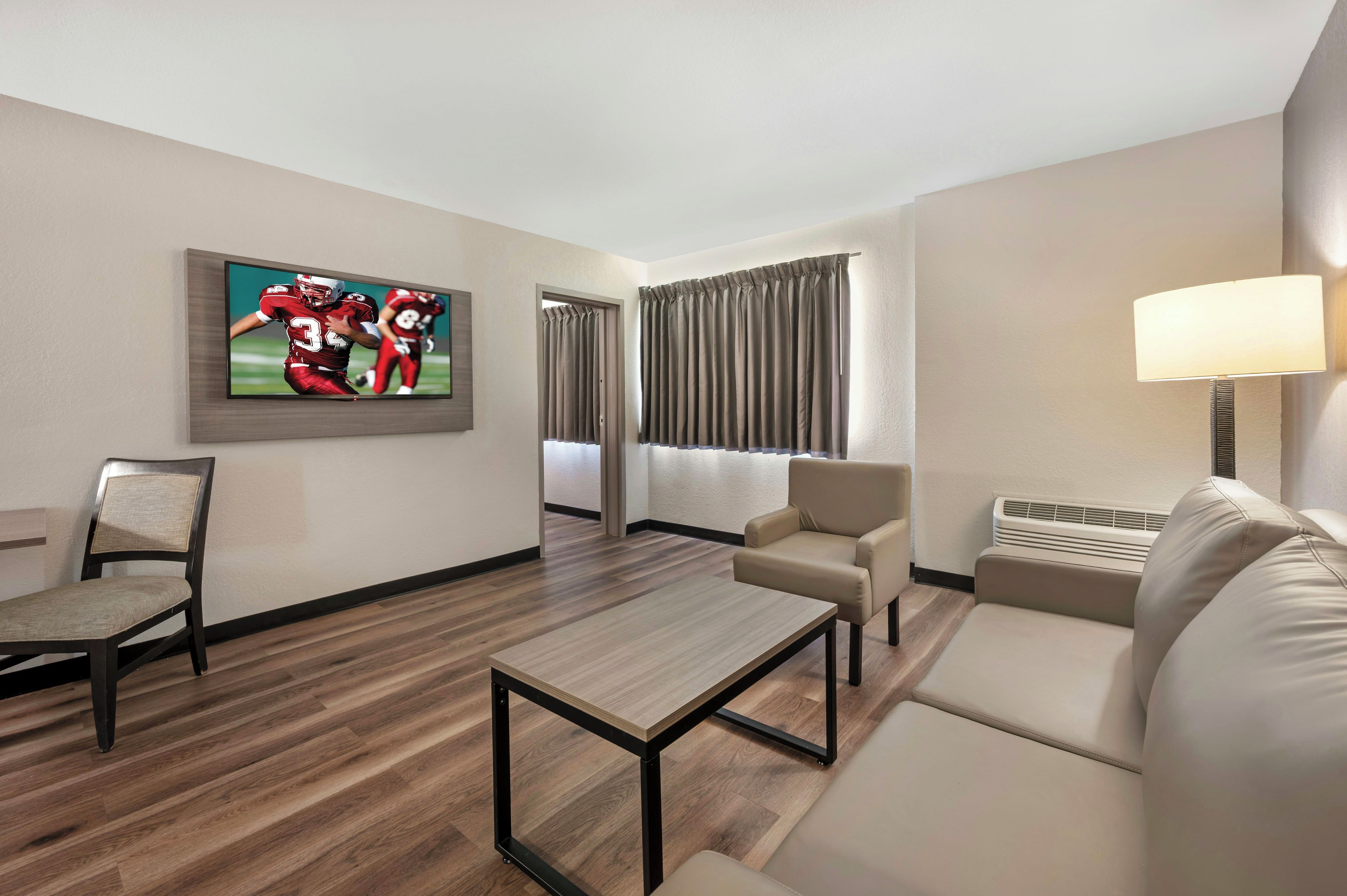 A hotel room with a flat-screen TV, a sofa, a chair, a coffee table, and a lamp.