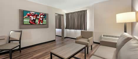 Habitación de hotel con televisor de pantalla plana, sofá, sillón, mesa de centro y lámpara.