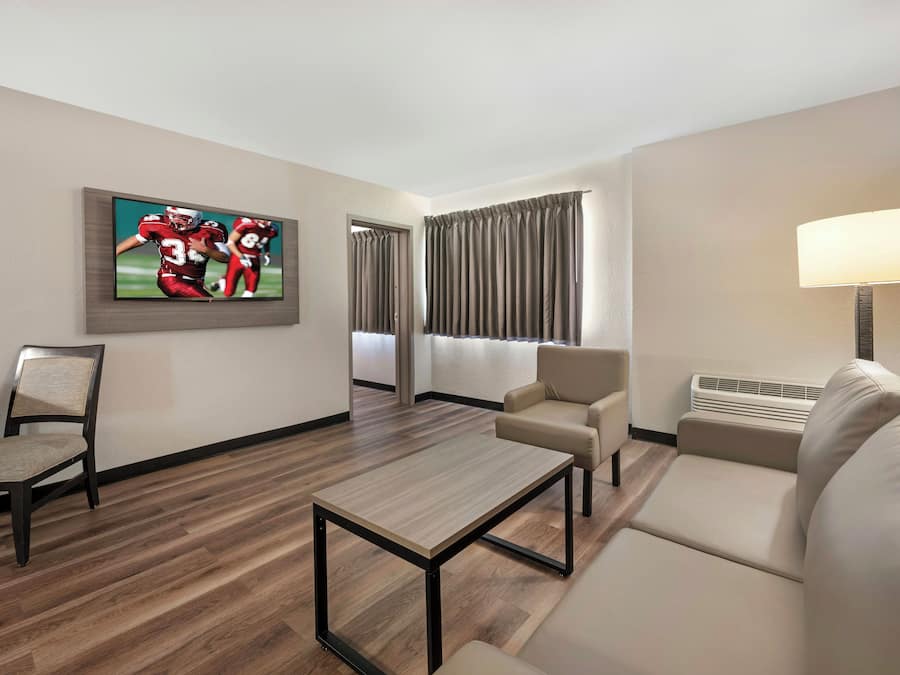 A hotel room with a flat-screen TV, a sofa, a chair, a coffee table, and a lamp.
