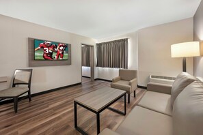Une chambre d’hôtel équipée d’un téléviseur à écran plat, d’un canapé, d’un fauteuil, d’une table basse et d’une lampe.