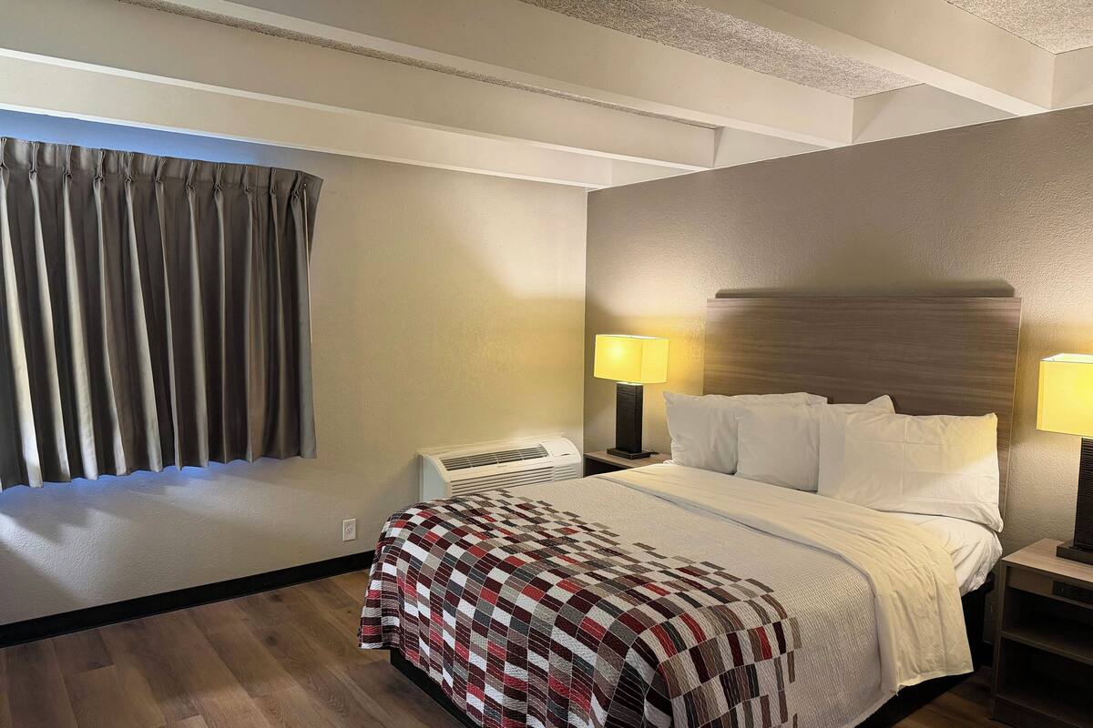 A hotel room with a bed, two bedside lamps, a telephone, and a window with curtains.