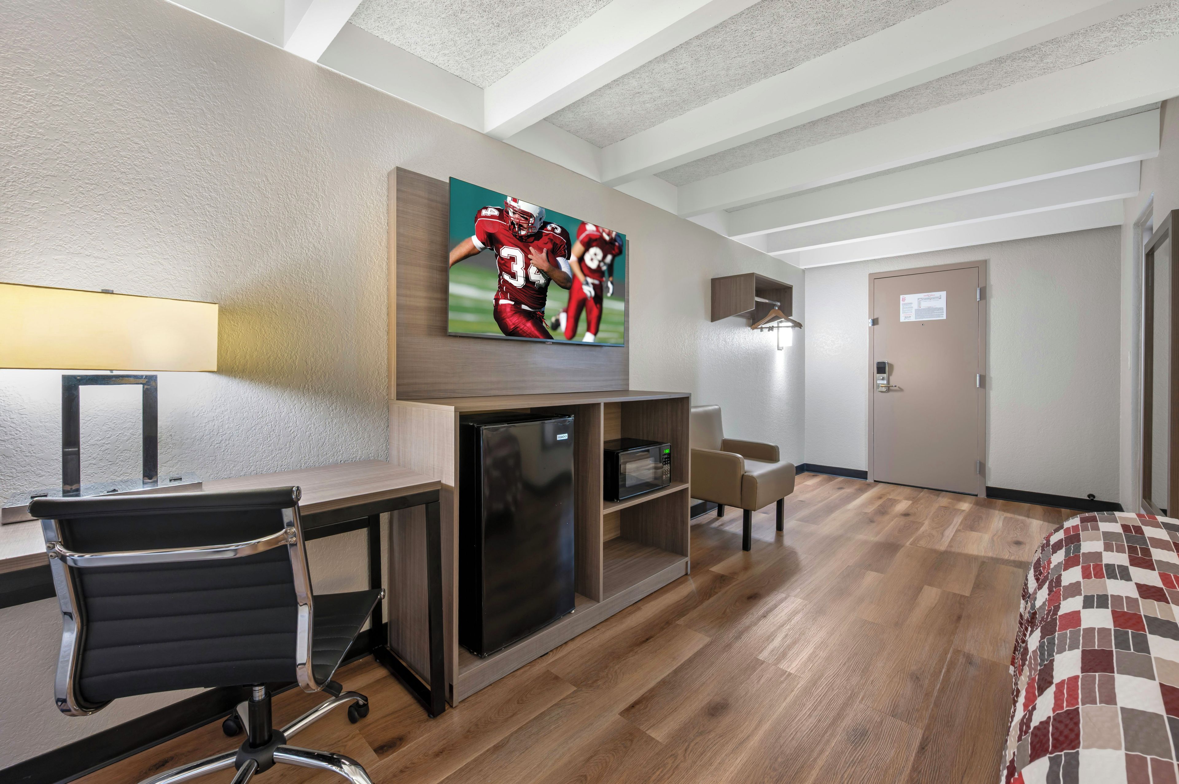 Habitación de hotel con cama, escritorio, silla, televisor, microondas y puerta.