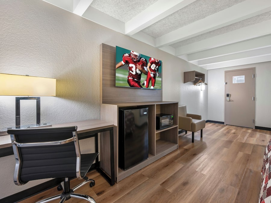 A hotel room with a bed, desk, chair, TV, microwave, and a door.