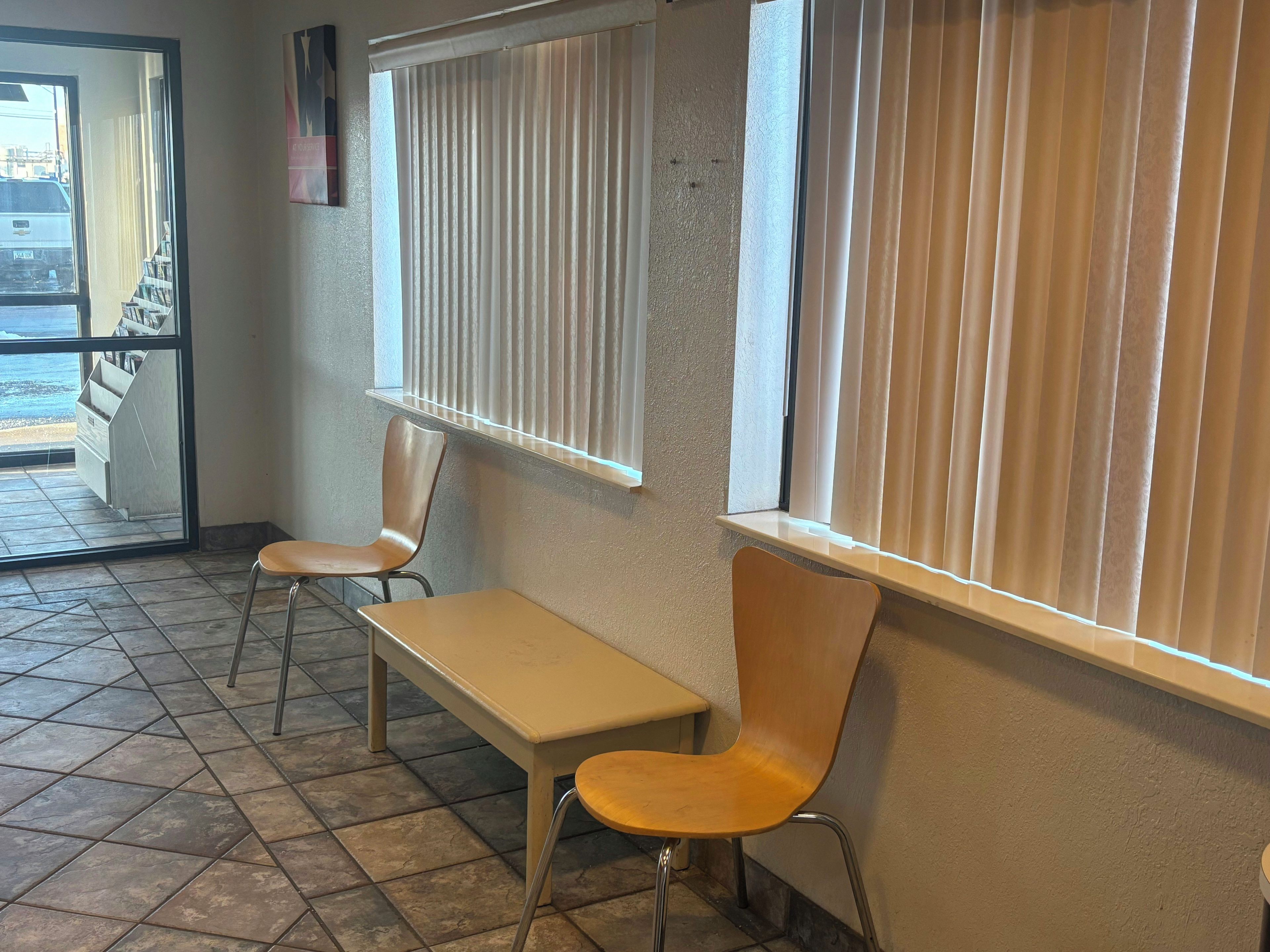 A waiting area with a bench and two chairs, a tiled floor, and a window with blinds.