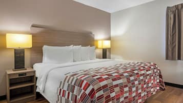 A hotel room with a bed, two bedside lamps, a wooden nightstand, and a quilt.