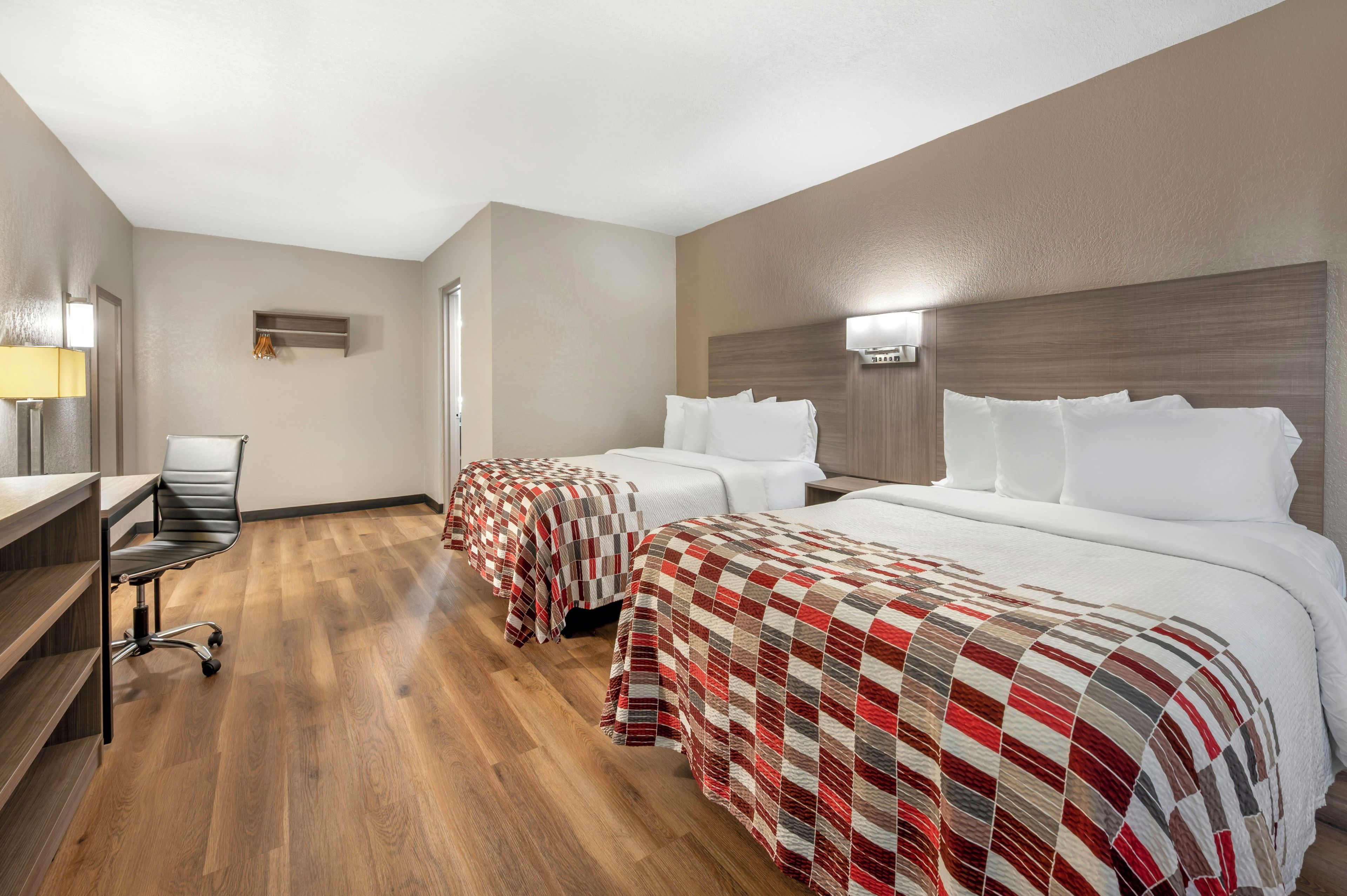 A hotel room with two beds, a desk, and a chair.