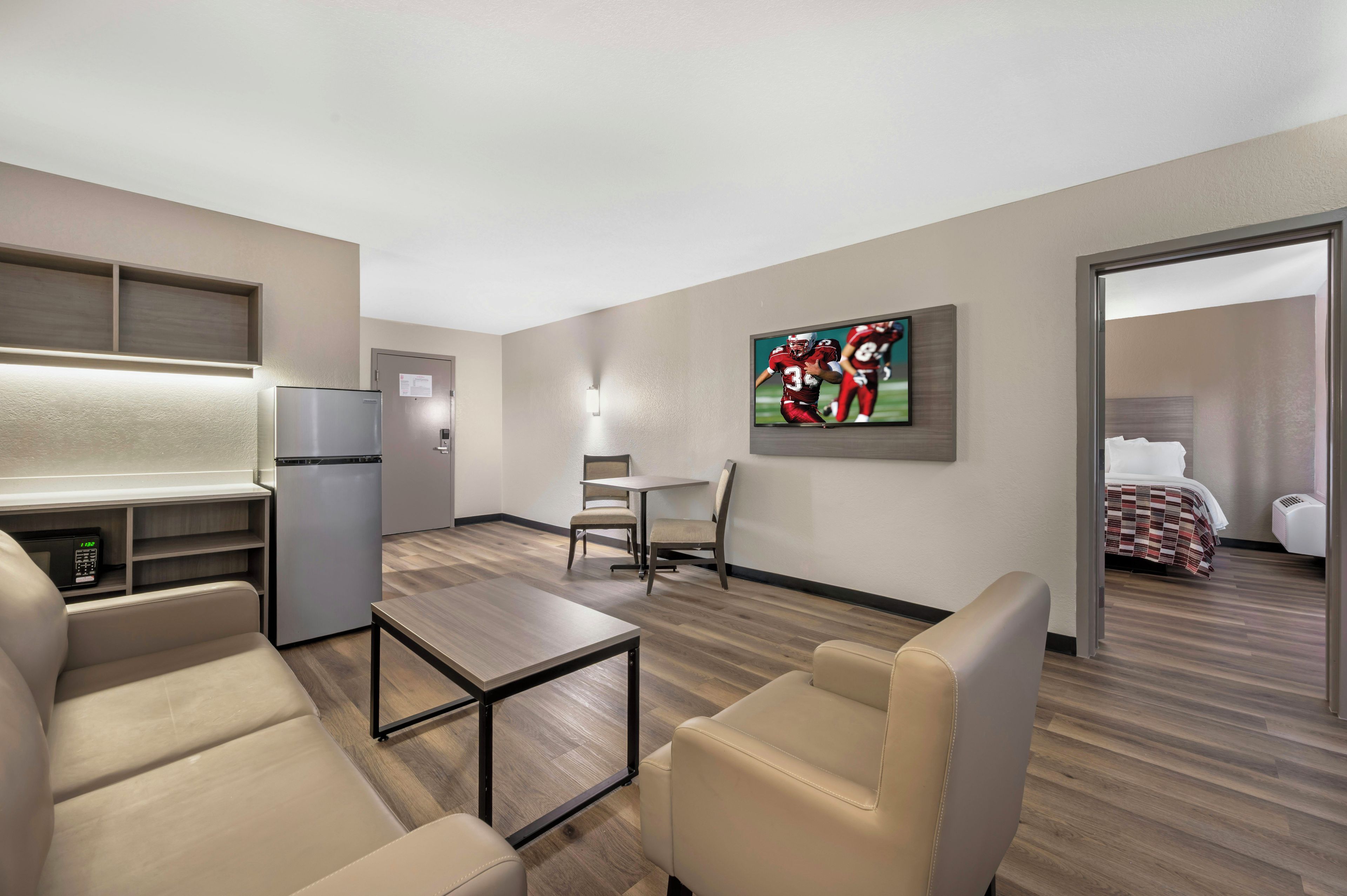 Une chambre d’hôtel dotée d’une kitchenette, d’un coin repas avec une table et des chaises, d’un téléviseur fixé au mur et d’un lit recouvert d’une couvre-lit à motifs.