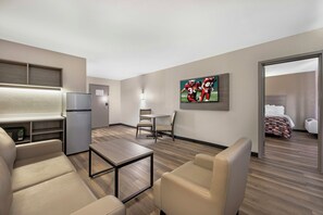 A hotel room with a kitchenette, a dining area with a table and chairs, a TV mounted on the wall, and a bed with a patterned bedspread. - Red Roof Inn Kokomo  (Kokomo)
