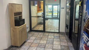 A hallway with a wooden cabinet, a glass door leading to a room, and a refrigerator. - Red Roof Inn Kokomo (Kokomo)