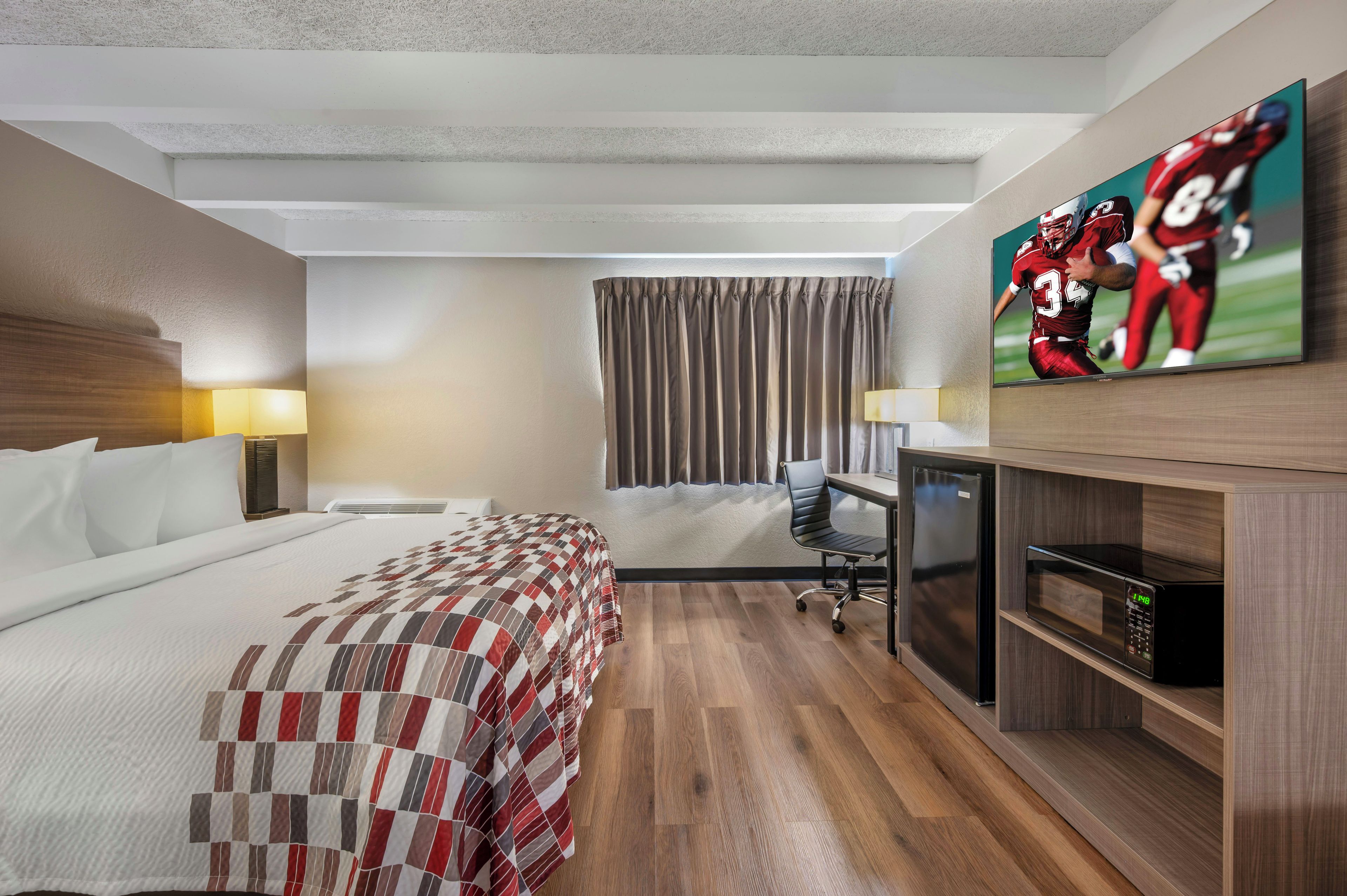 A hotel room with a bed, a desk, a television, and a microwave.