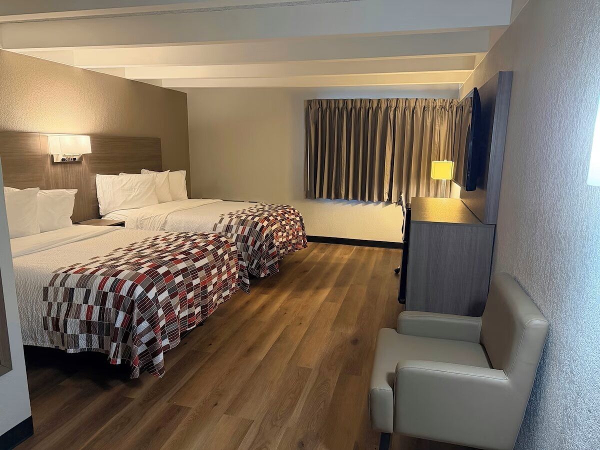 A hotel room with a bed, a chair, a TV, and a window with curtains.