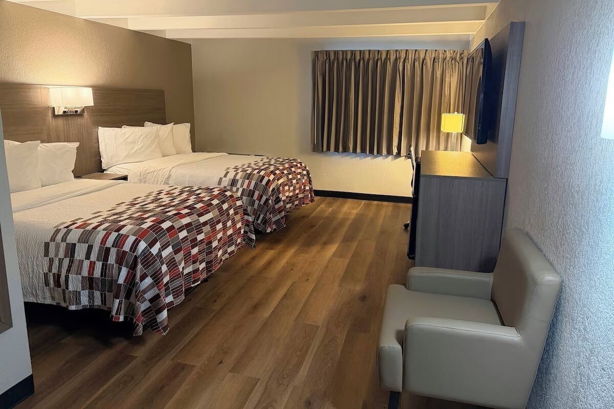 A hotel room with a bed, a chair, a TV, and a window with curtains.