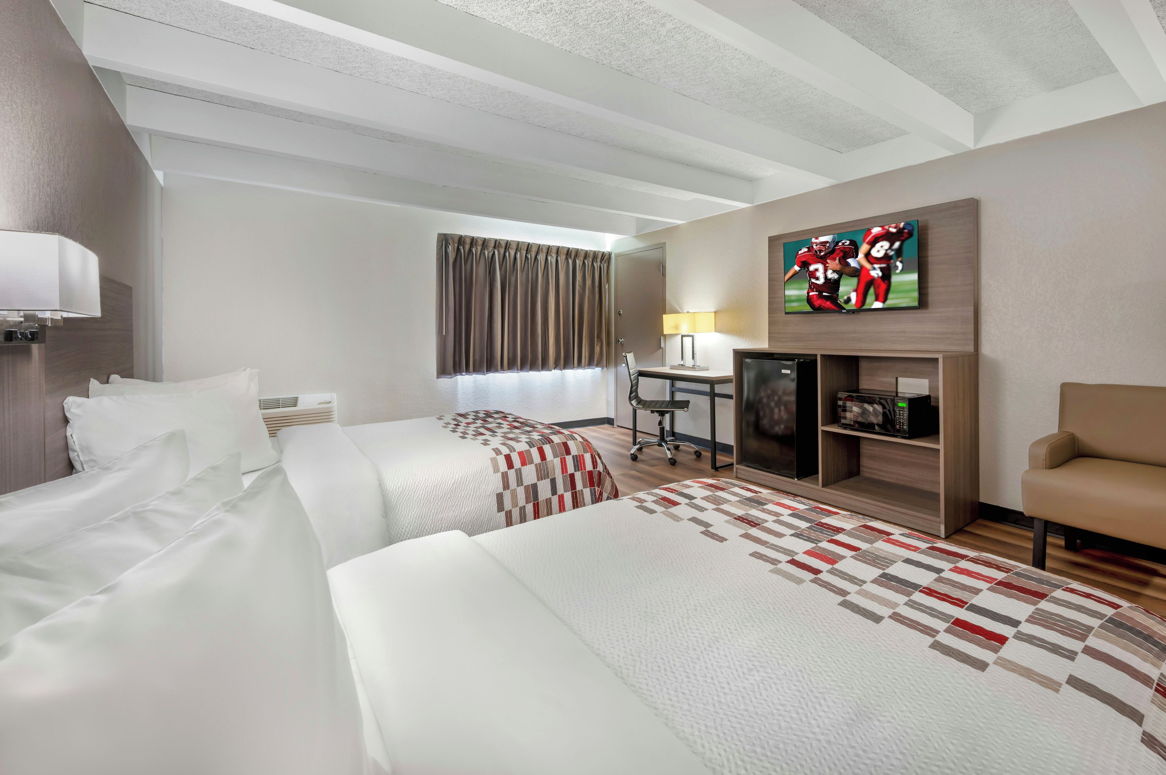 Ein Hotelzimmer mit zwei Betten, einem Schreibtisch, einem Fernseher und einem Sofa.