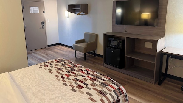 A hotel room with a bed, a TV, a microwave, a chair, and a minibar. - Red Roof Inn Kokomo (Kokomo)