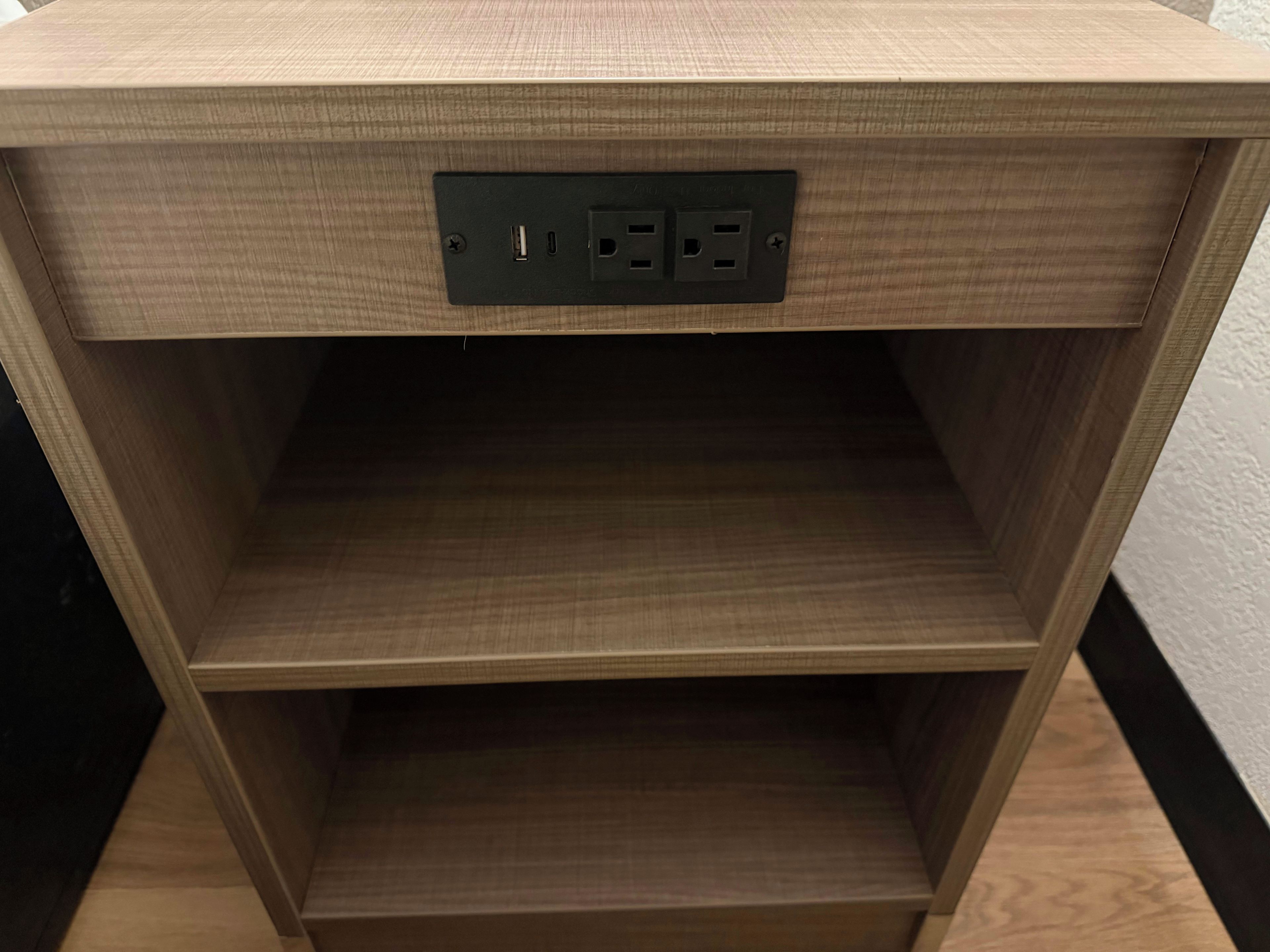 Ein Nachttisch aus Holz mit ebener Oberfläche und einem Steckdosenanschluss.