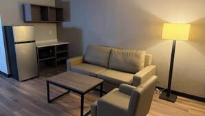 A compact living space with a sofa, a coffee table, a lamp, a kitchenette, and a small cabinet. - Red Roof Inn Kokomo (Kokomo)