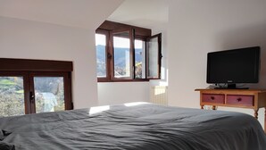 Ein Schlafzimmer mit einem großen Bett, einem Fernseher auf einem Holzboden, einem Fenster mit Bergblick und einer Heizung.