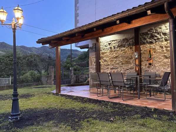 An outdoor patio with a stone wall, a wooden pergola, and a table with chairs.