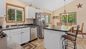 A modern kitchen with white cabinets, a stainless steel refrigerator, a dishwasher, and a bar area with two stools.