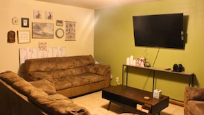 Ein Wohnzimmer mit einer braunen Couch, einem Couchtisch und einem an einer grünen Wand montierten Flachbildfernseher.