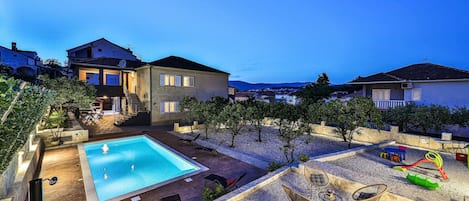 A residential area with a swimming pool, outdoor seating, and a view of the surrounding neighborhood.