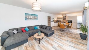 A modern living room with a sectional sofa, a round coffee table, and a dining area with a table and chairs. - Lovely apartment in Okrug Gornji (Okrug Gornji)
