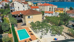 A residential area with a swimming pool, surrounded by houses with red-tiled roofs, and a view of the sea in the background. - Lovely apartment in Okrug Gornji (Okrug Gornji)