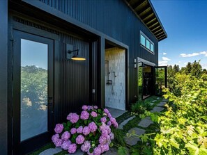 A modern house with a large glass door, a small window, and a garden with pink flowers. - Vineyard Daydream - Villa with Wine Tastings Included (Healdsburg)