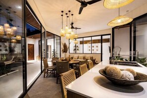 A modern interior with a dining area, a large window, and a ceiling fan. - Villa Jungle Rendez Vous by BaliSuperHost (Bali)