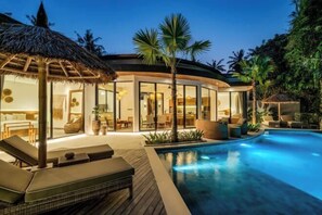 Un resort moderno con piscina, zona de estar y vegetación tropical.