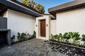 Fachada moderna con un patio empedrado, una puerta de madera y un pequeño jardín con plantas.