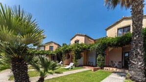 A courtyard with palm trees, a patio with chairs, and a building with a tiled roof. - Unique House in an Extraordinary Place (Pula)