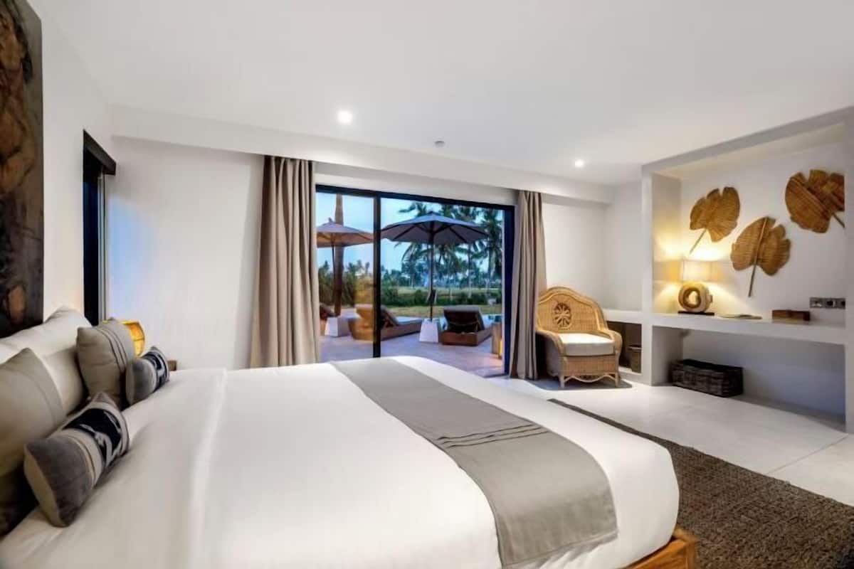 A modern hotel room with a large bed, a seating area with a view, and a wall with decorative leaves.