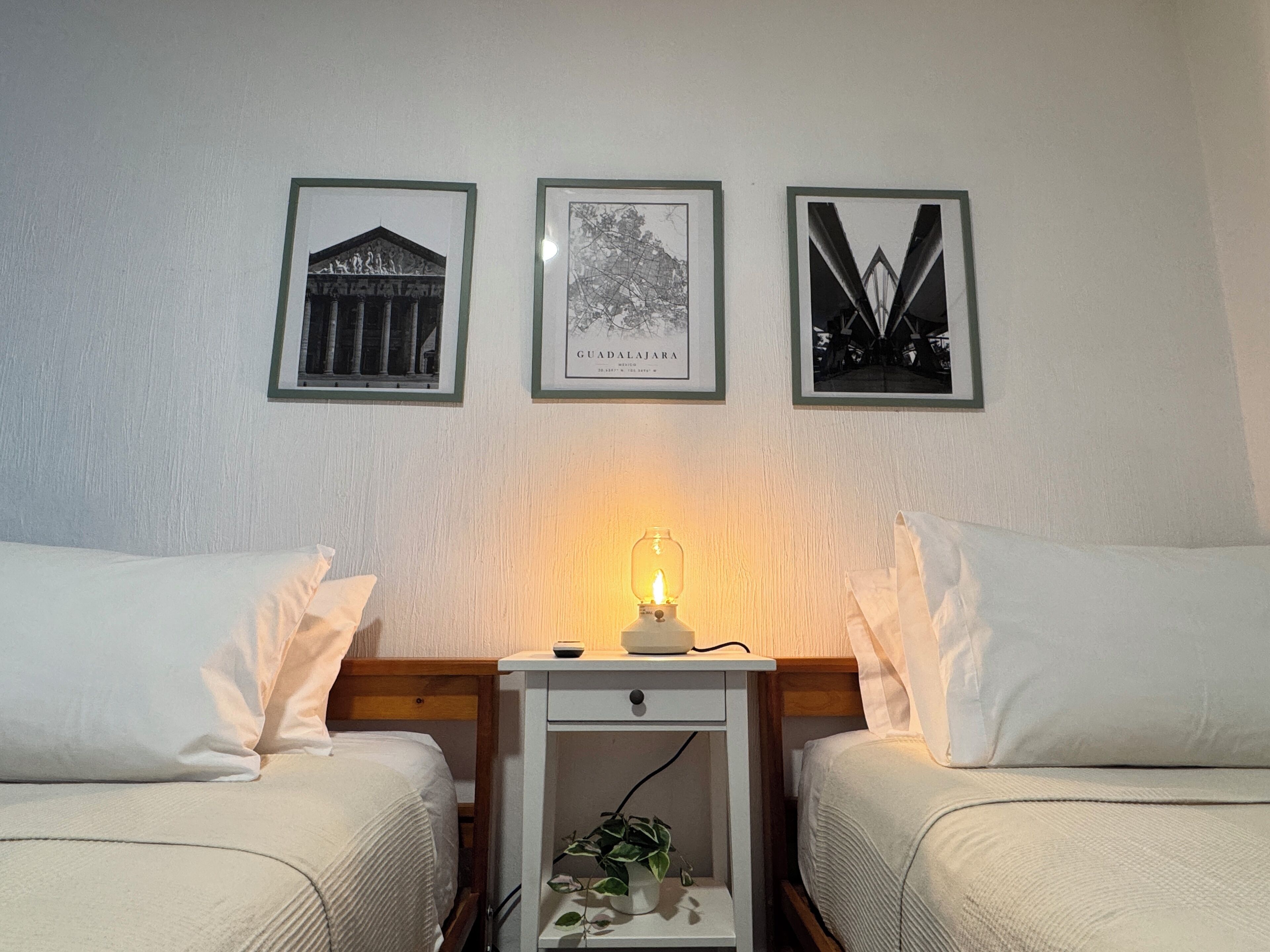 A room with two beds, a nightstand with a lamp, and three framed pictures on the wall.