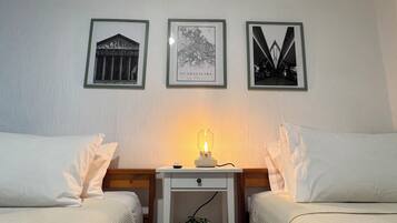 A room with two beds, a nightstand with a lamp, and three framed pictures on the wall.