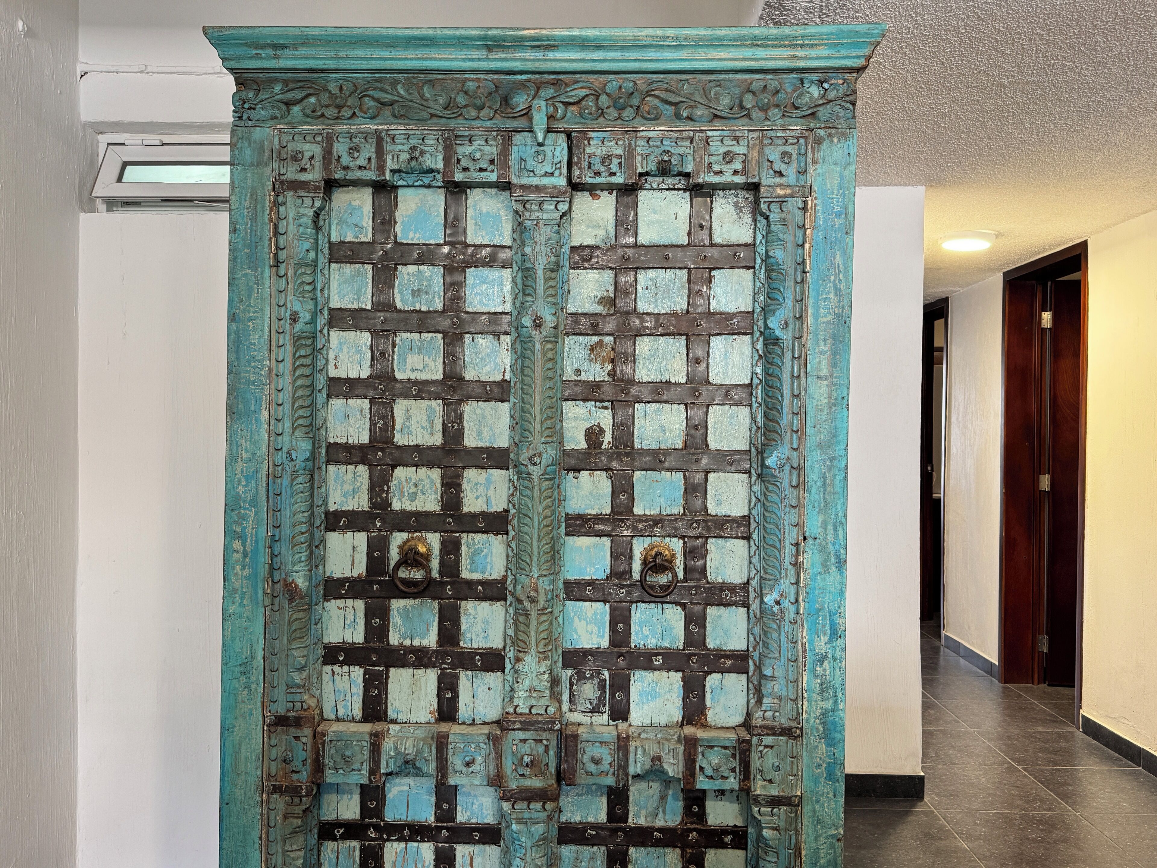 A hallway with a large, ornate door featuring a grid pattern and metal hinges.