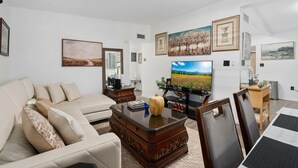 Ein Wohnzimmer mit Sofa, Couchtisch, Fernseher und gerahmten Kunstwerken an den Wänden.