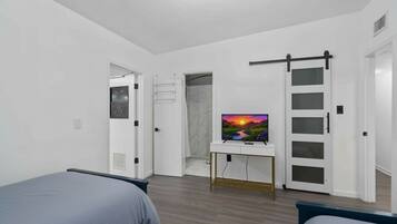 A modern bedroom with two beds, a TV on a white console, a sliding door, and a shower area.