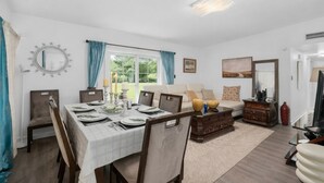 Ein Essbereich mit Tisch für vier Personen, einer Couch und einem Couchtisch in einem Zimmer mit weißen Wänden und einem großen Fenster.