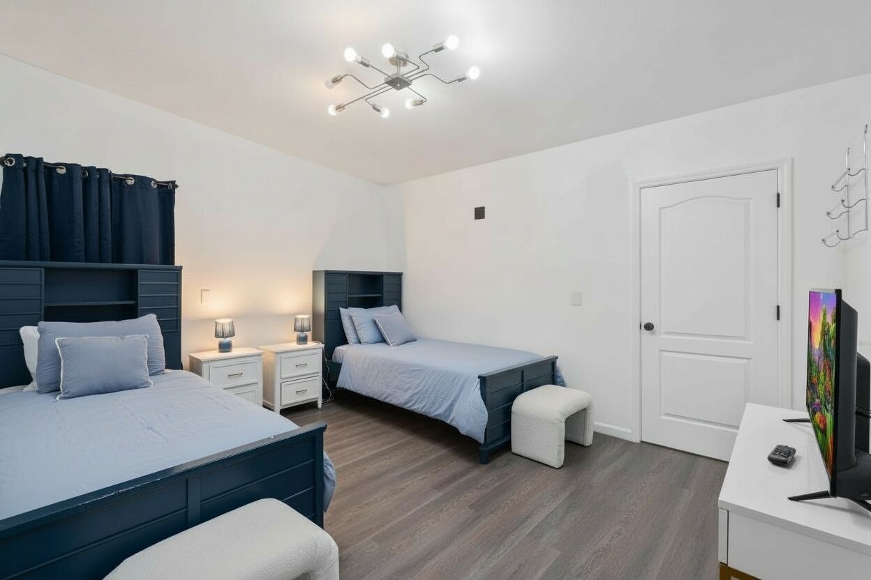 Une chambre avec deux lits, un bureau, une télévision et un luminaire au plafond.