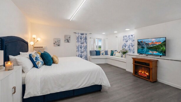 Ein Schlafzimmer mit Bett, Nachttisch, Lampe, Fernseher, Kamin und einem Fenster mit Vorhängen.