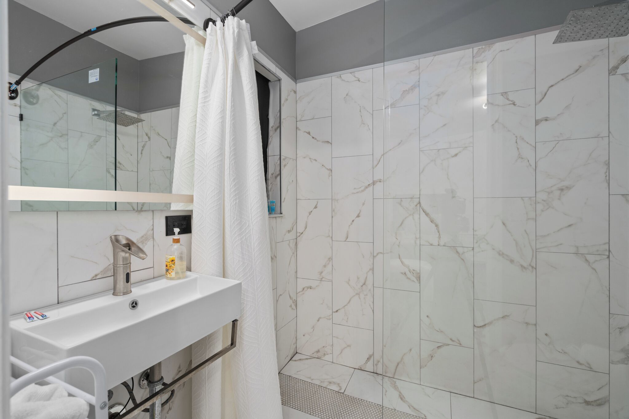A bathroom with a shower, a sink with a mirror, and a towel rack.