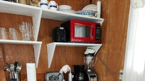 Una cocina compacta con armarios de madera, un fregadero, un microondas rojo, una cafetera y una licuadora.