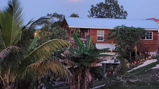 Una casa con techo rojo y un porche, rodeada de exuberante vegetación tropical.