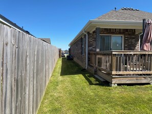 Ein eingeschossiges Haus mit überdachter Veranda, einem eingezäunten Garten und blauem Himmel.