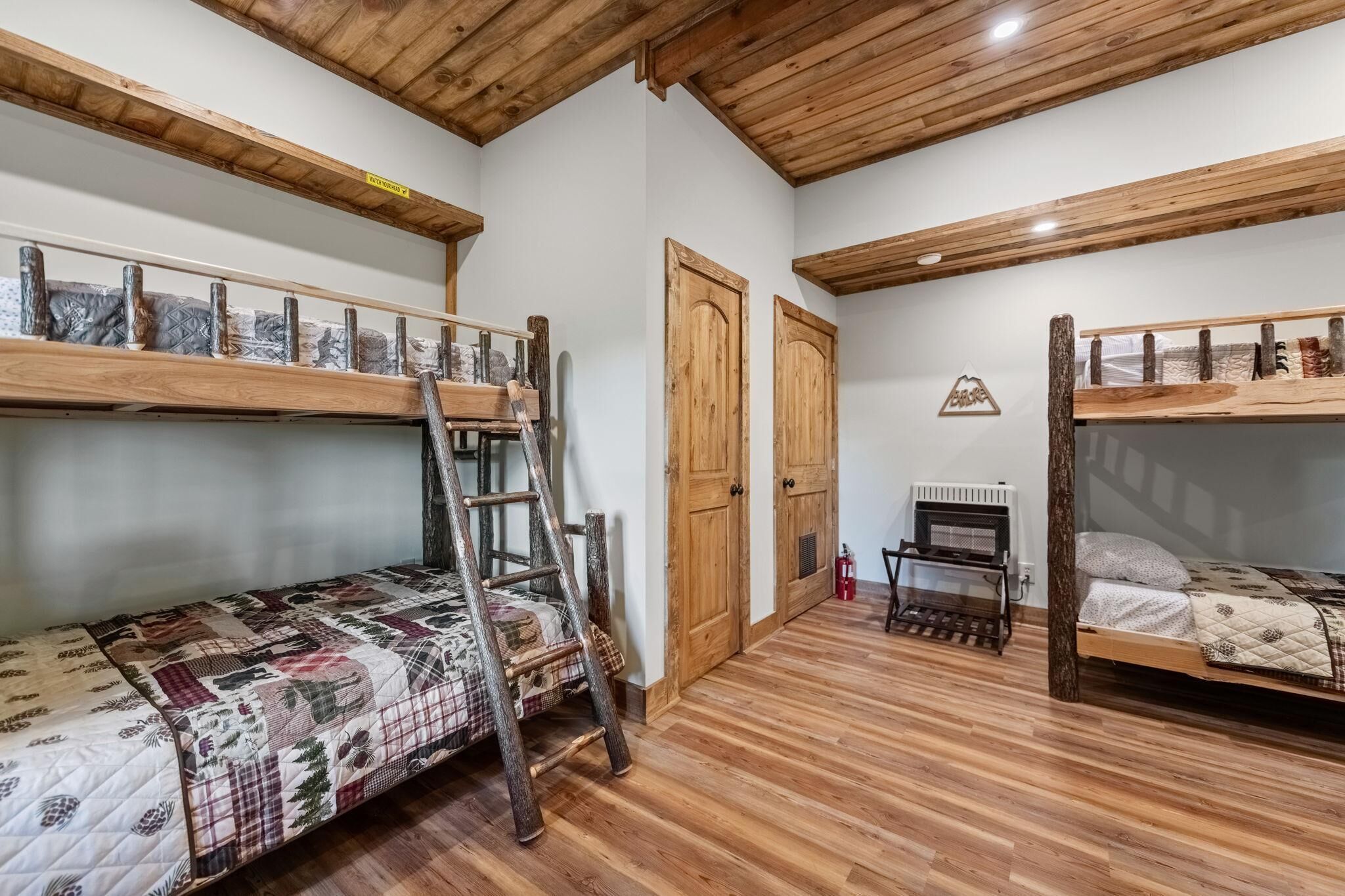 Een kamer met twee stapelbedden, houten vloeren, een ladder, een radiator en een klein tafeltje.