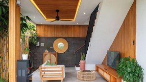 A modern living room with a wooden ceiling, a black entertainment unit, a round wall decoration, and a staircase. - Paz Tropical Villa Ubud by Omkara Experience (Bali)